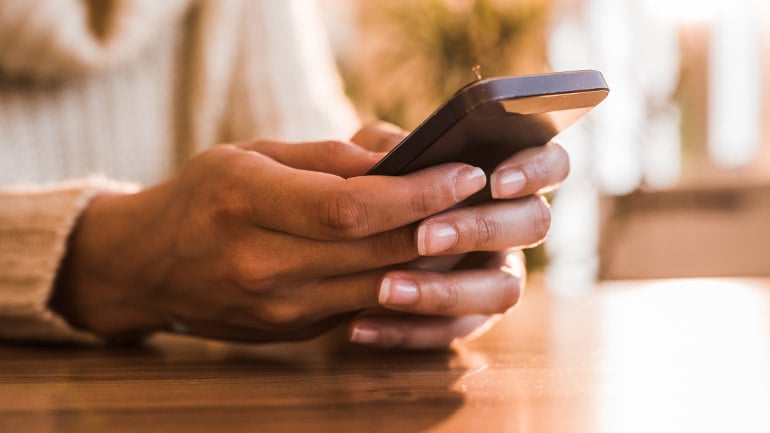 A woman holds a mobile phone and reads the news.